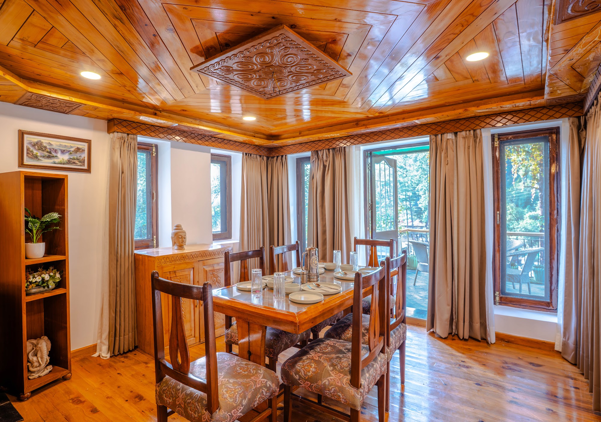 Dining table in the Hall Balcony Suite under a wooden ceiling, with windows onto the trees
